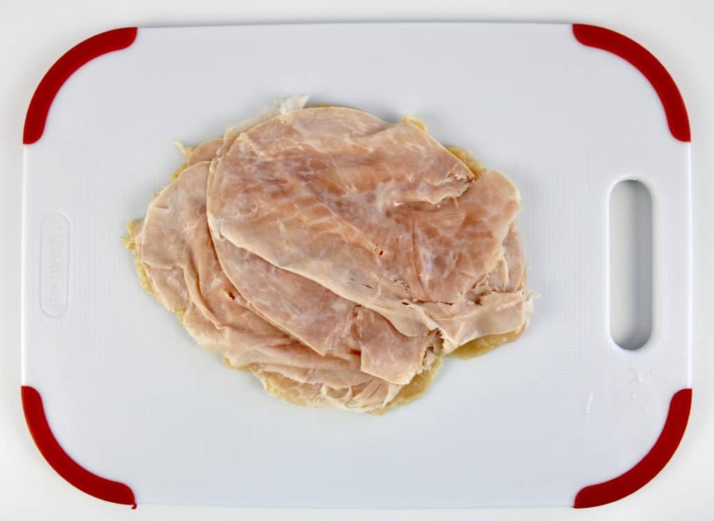 ham slices on top of chicken on cutting board