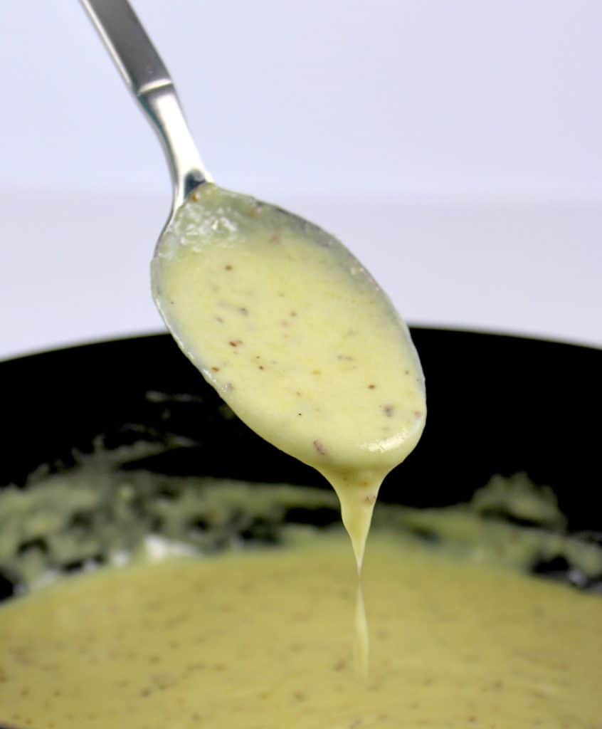 mustard cheese sauce in saucepan with spoon holding up some