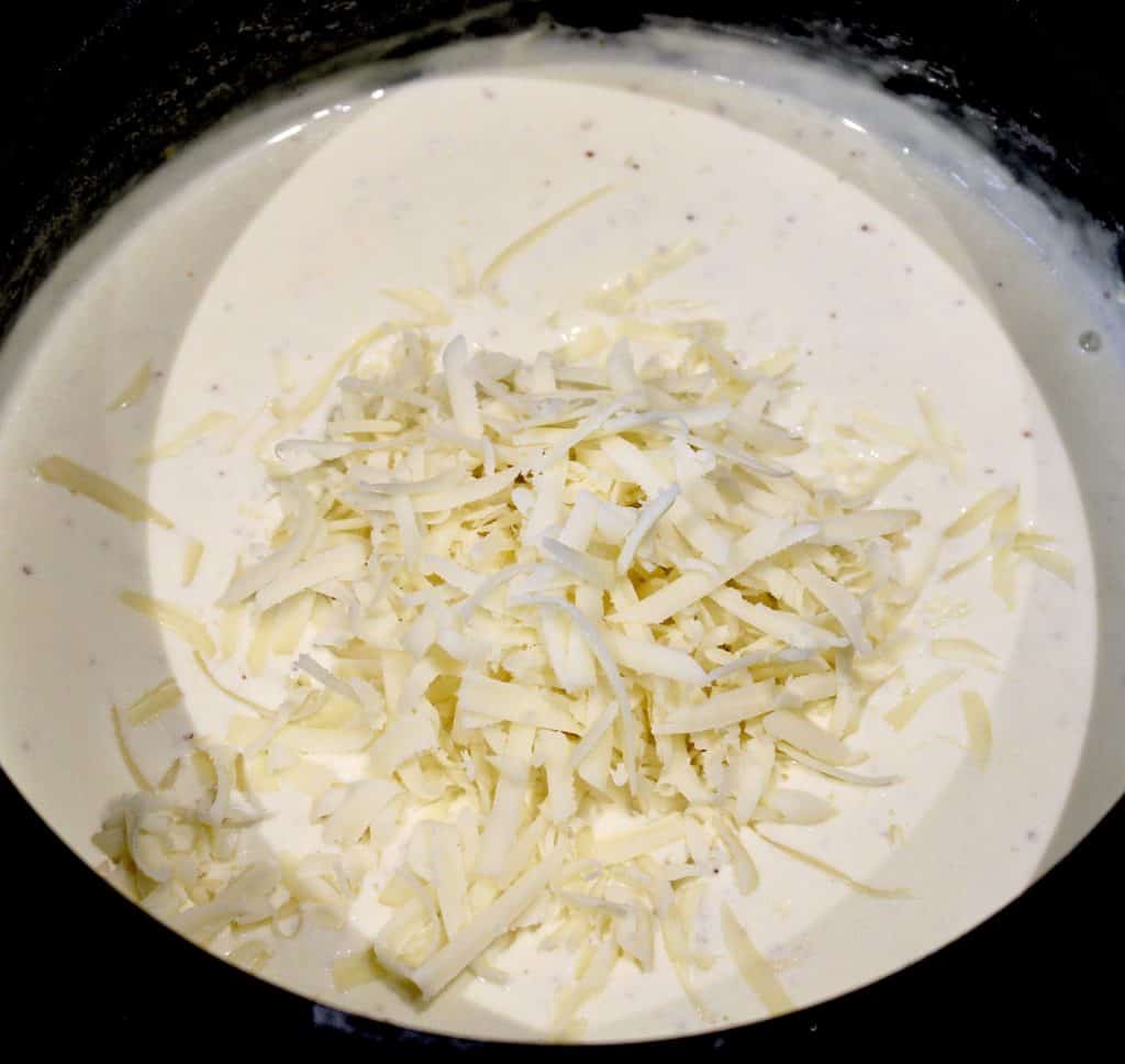 cream sauce in saucepan with shredded cheese on top