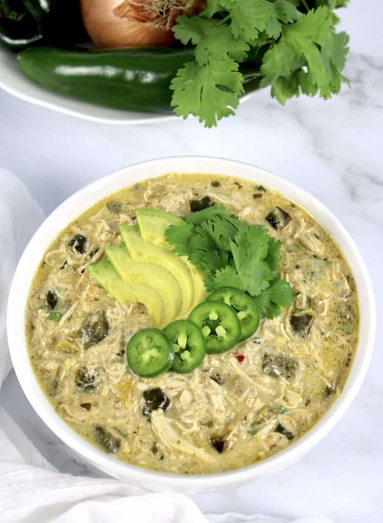 overhead view of bowl of white chicken chili with sliced avocado jalapeno and cilantro on top