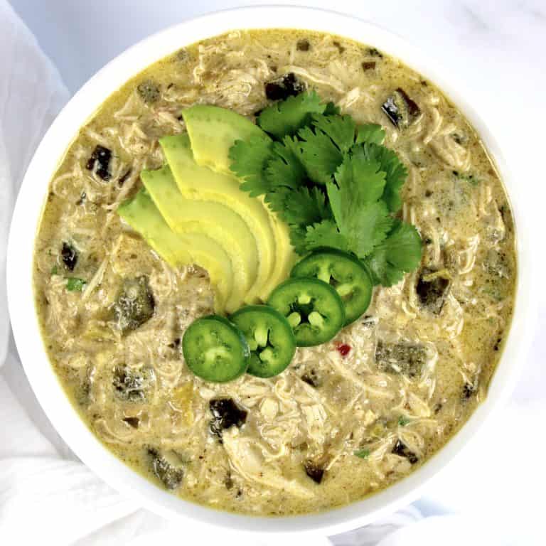 overhead view of bowl of white chicken chili with sliced avocado jalapeno and cilantro on top
