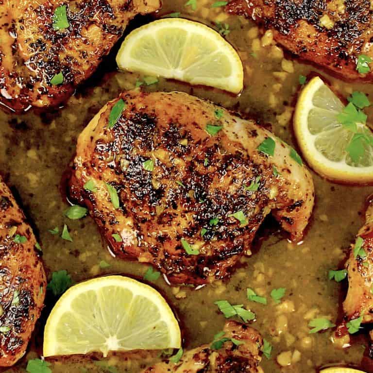 pieces of Lemon Chicken in skillet with sauce and lemon slices