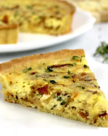 closeup of slice of quiche lorraine on white plate with rest of quiche in background