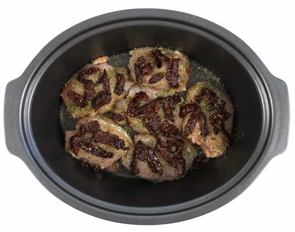 raw chicken with sun dried tomatoes on top in crockpot insert