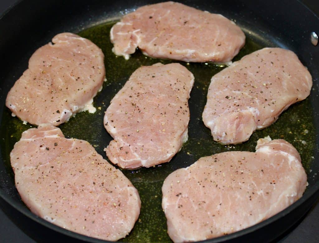 6 raw pork chop in skillet with salt and pepper on top