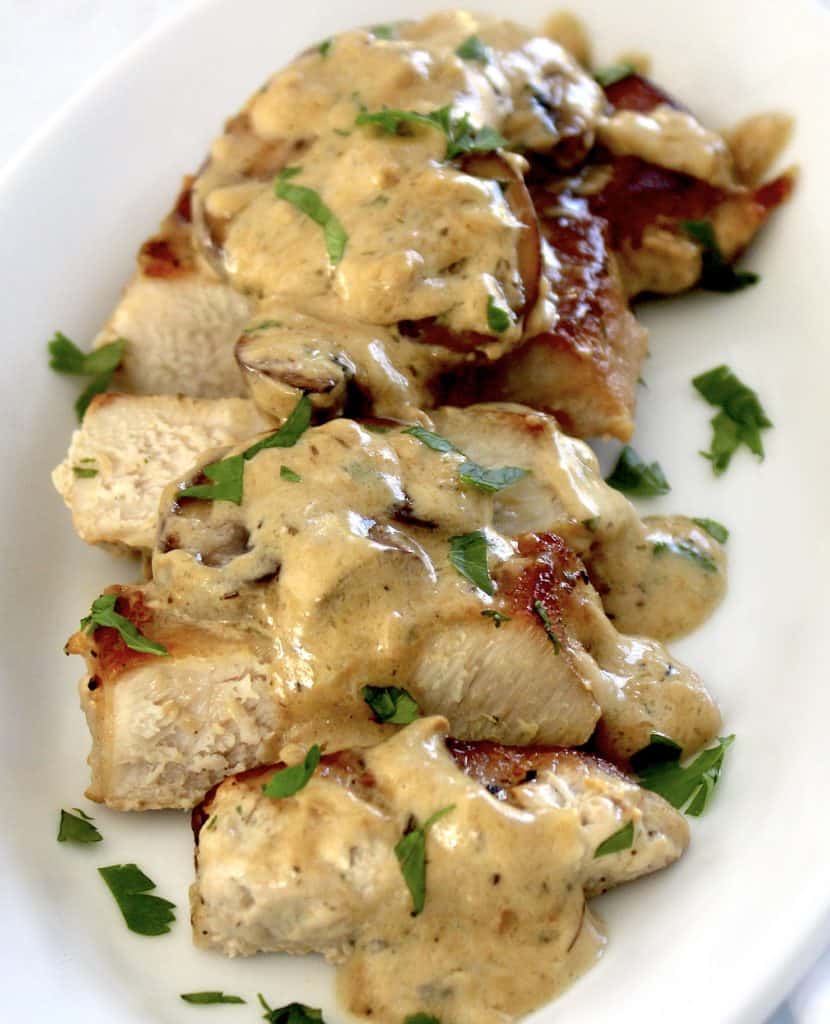 sliced pork chop with mushroom gravy over the top on white plate
