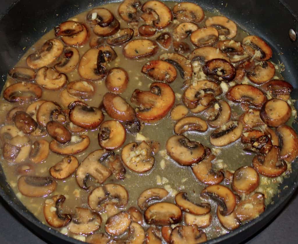 cooked mushrooms and garlic with chicken broth in skillet