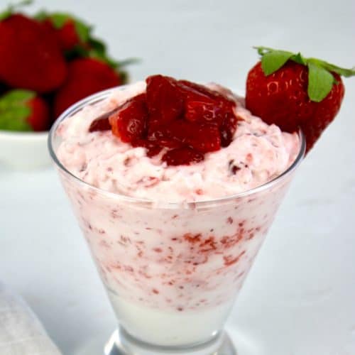 Strawberries and Cream in glass bowl with strawberry on side of glass and strawberries in background