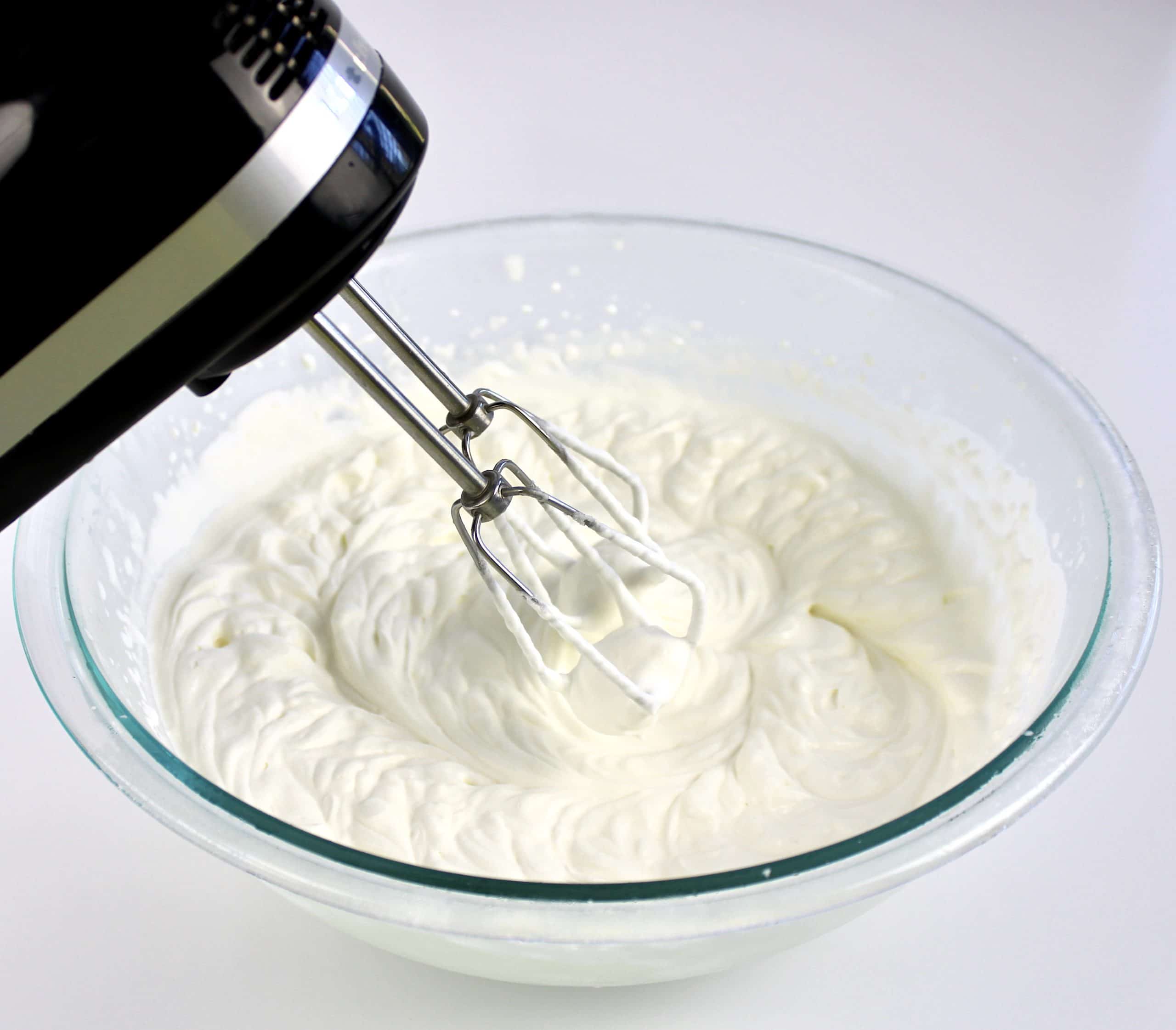 whipped cream in glass bowl with hand mixer