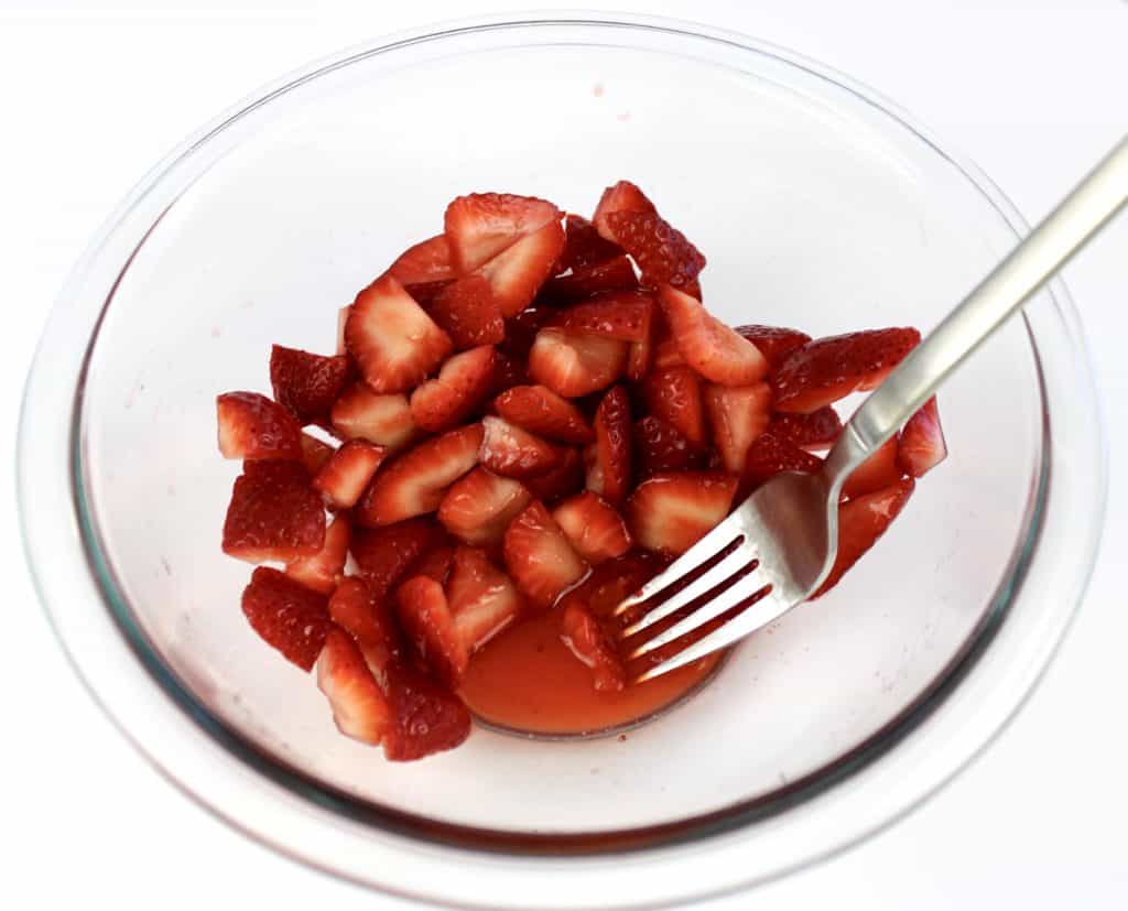 chopped strawberries in bowl with fork mashing them