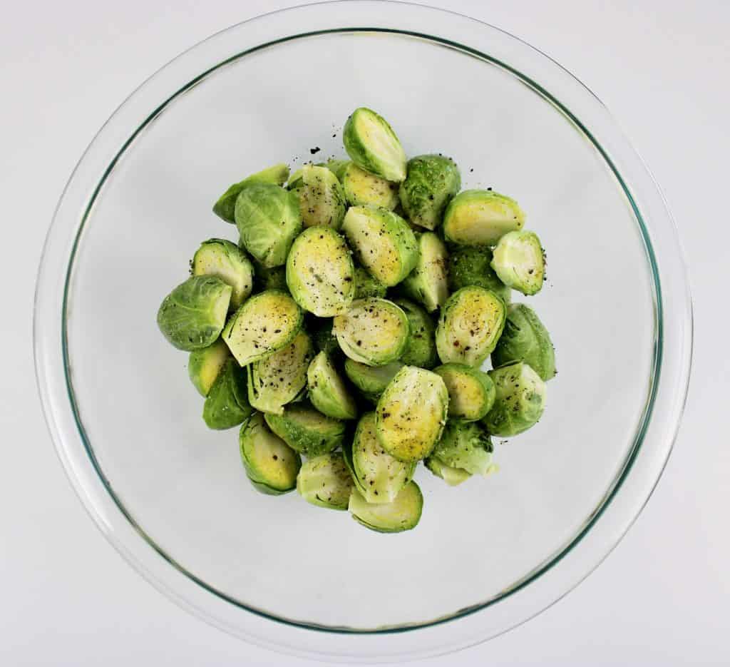 Brussels sprouts cut in half in glass bowl with salt pepper olive oil