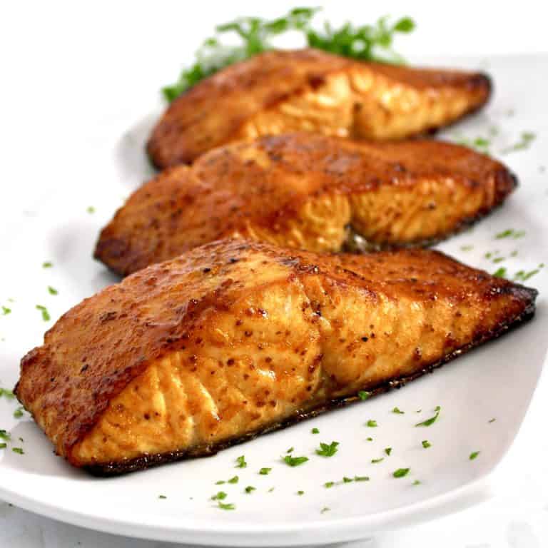 3 pieces of cooked salmon on white plate with parsley garnish