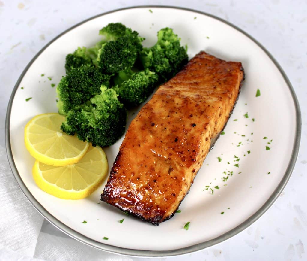 piece of glazed salmon on white plate with broccoli and 2 slices of lemon