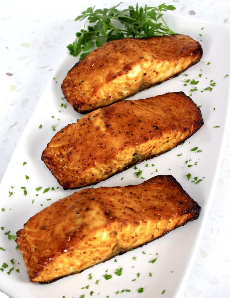 3 pieces of cooked salmon on white plate with parsley garnish