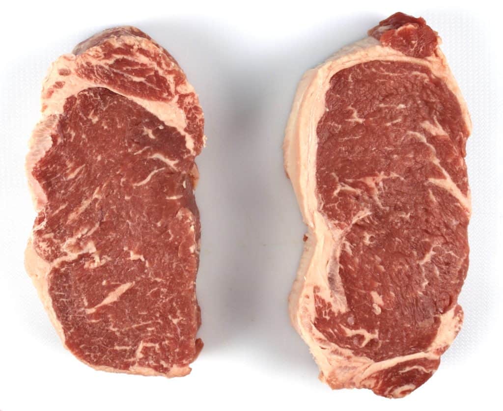 2 NY strip steaks on white cutting board