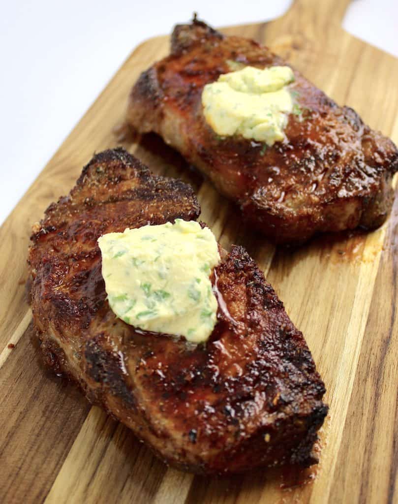 2 Air Fryer Steaks on cutting board with compound butter pads on top