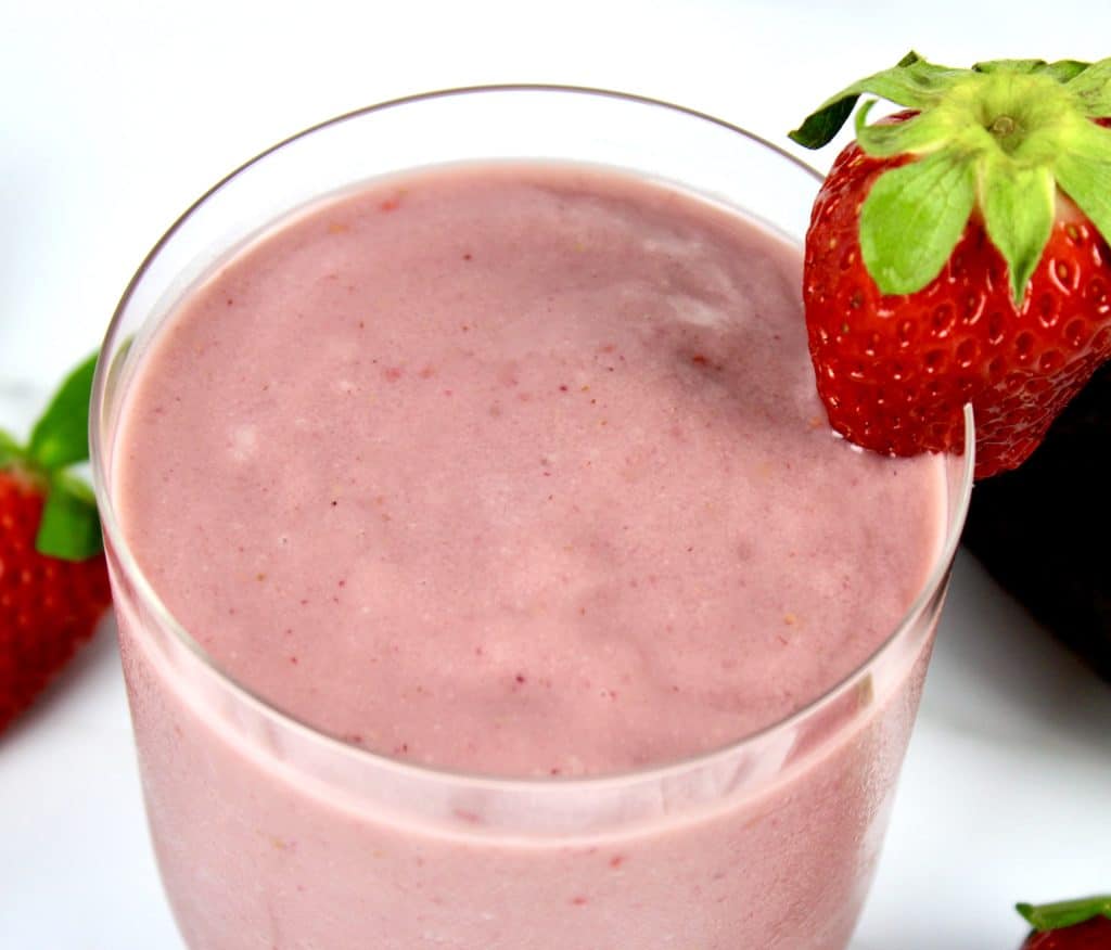 closeup overhead view of berry avocado smoothie in glass with strawberry on side of glass