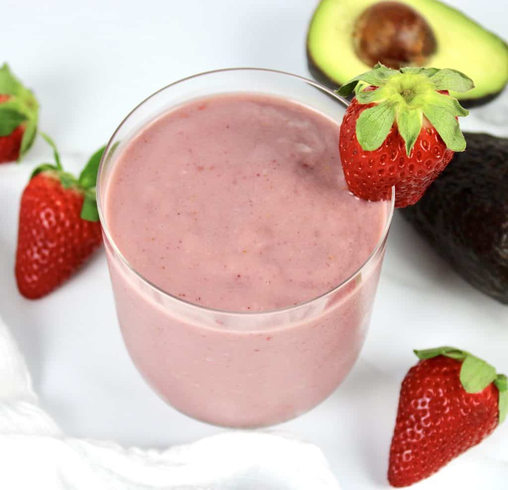 overhead view of berry avocado smoothie in glass with strawberry on side of glass