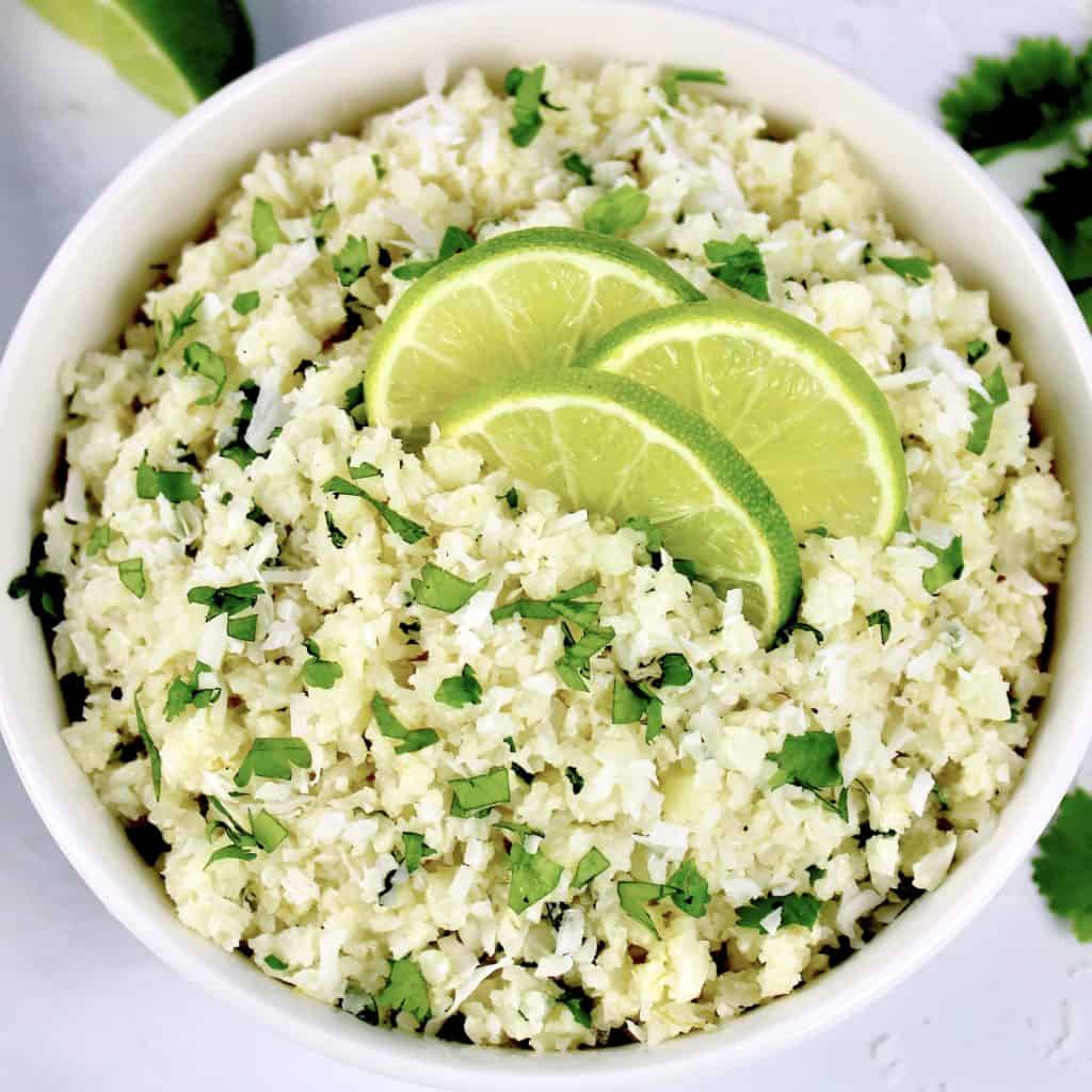 Coconut Cauliflower Rice in white bowl with 3 lime slices on top