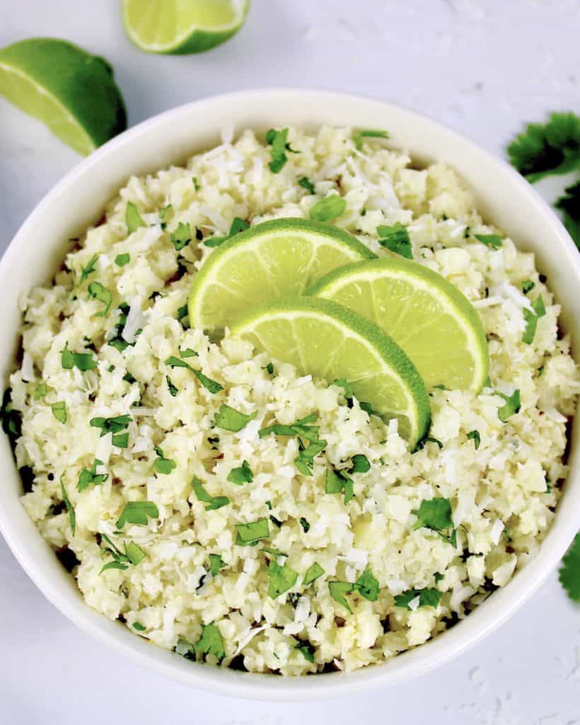overhead view of Coconut Cauliflower Rice in white bowl with lime slices on top