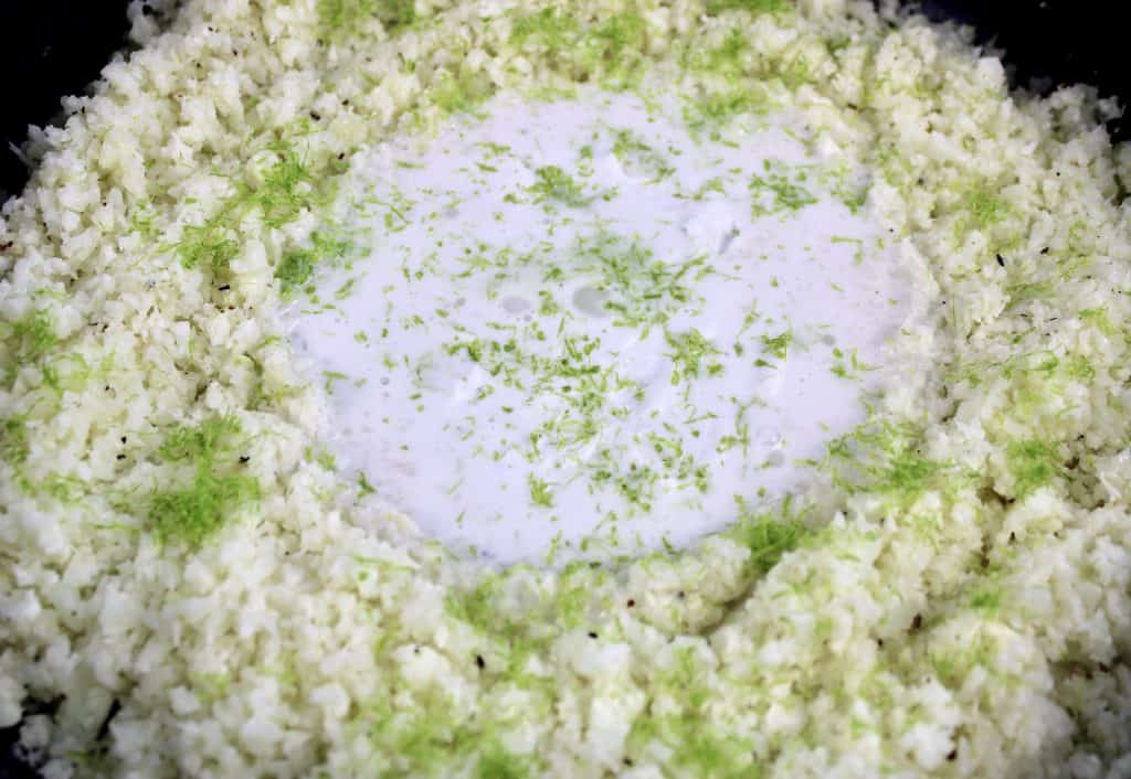 cauliflower rice in skillet with coconut cream in center and lime zest on top