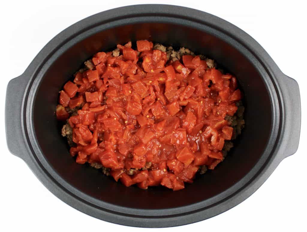 ground beef and chopped tomatoes on top in crockpot insert