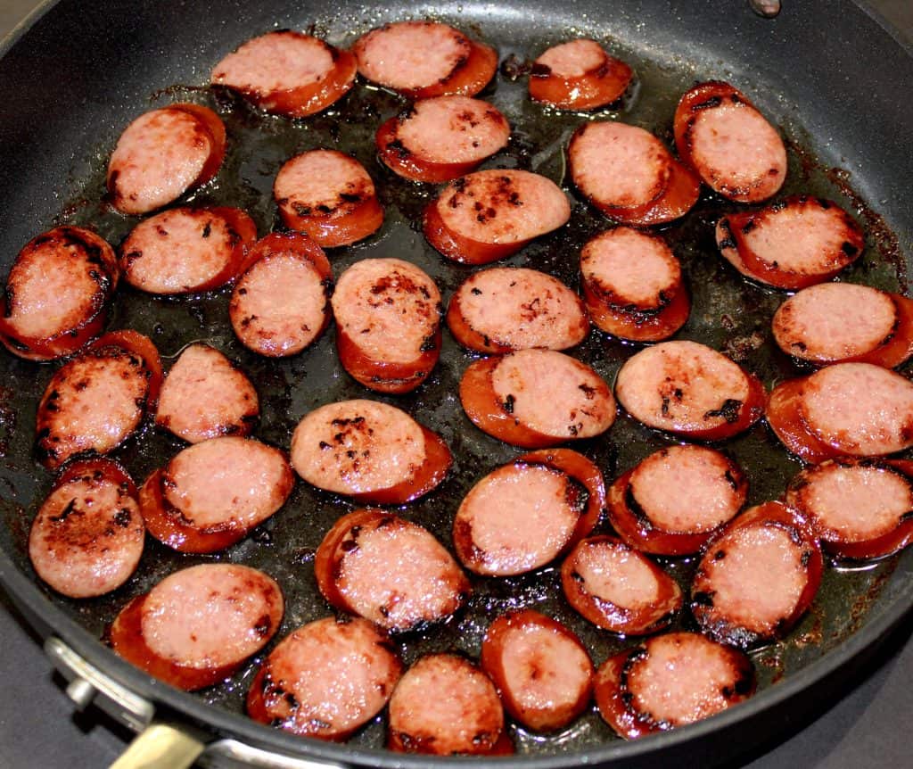 slices of smoked sausage frying in skillet