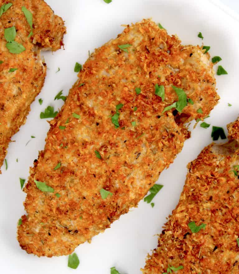 overhead view of breaded pork chops on white plate with parsley
