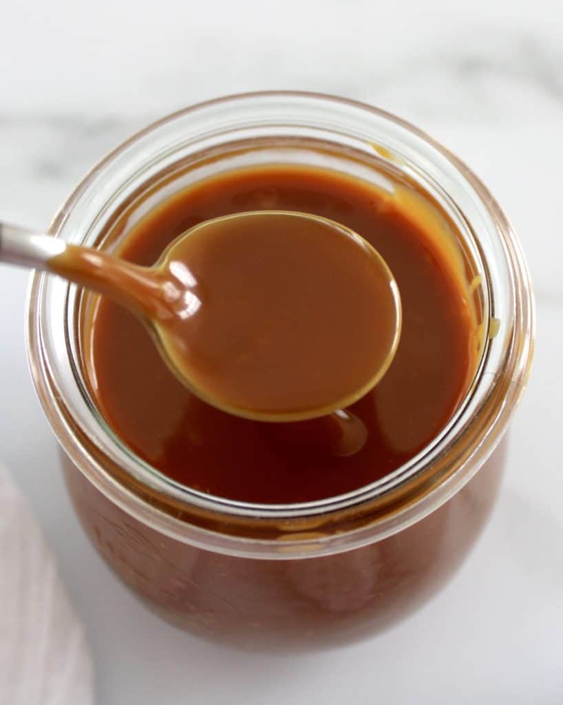 overhead view of Salted Caramel Sauce with spoon over glass jar