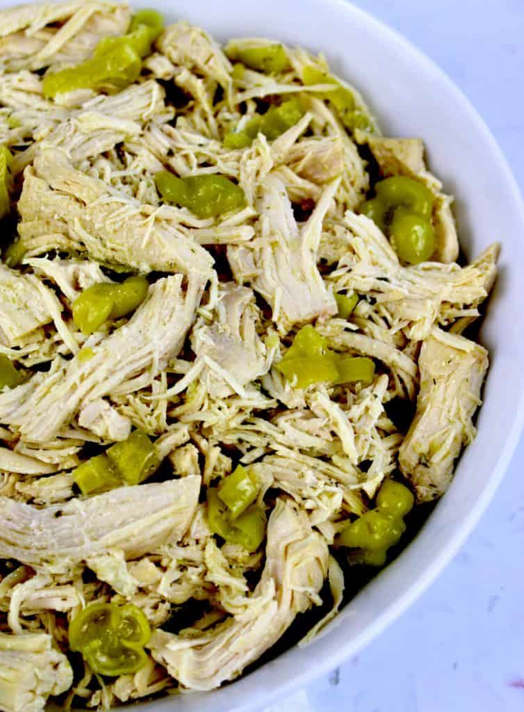 closeup of Mississippi chicken shredded in white bowl with slices of peppers