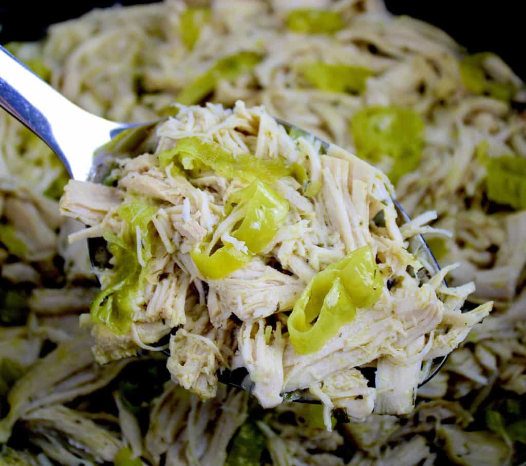 Shredded Mississippi chicken with sliced peppers held up by serving spoon