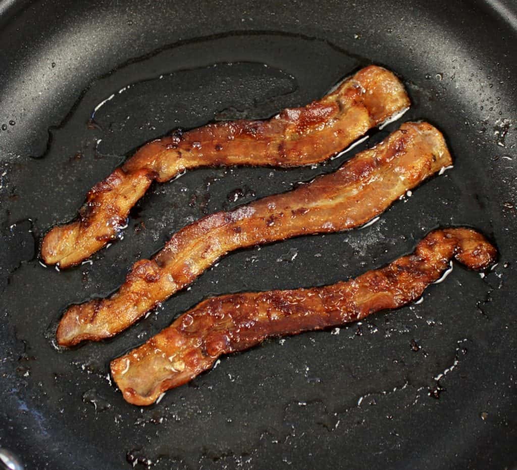 3 slices of bacon frying in skillet
