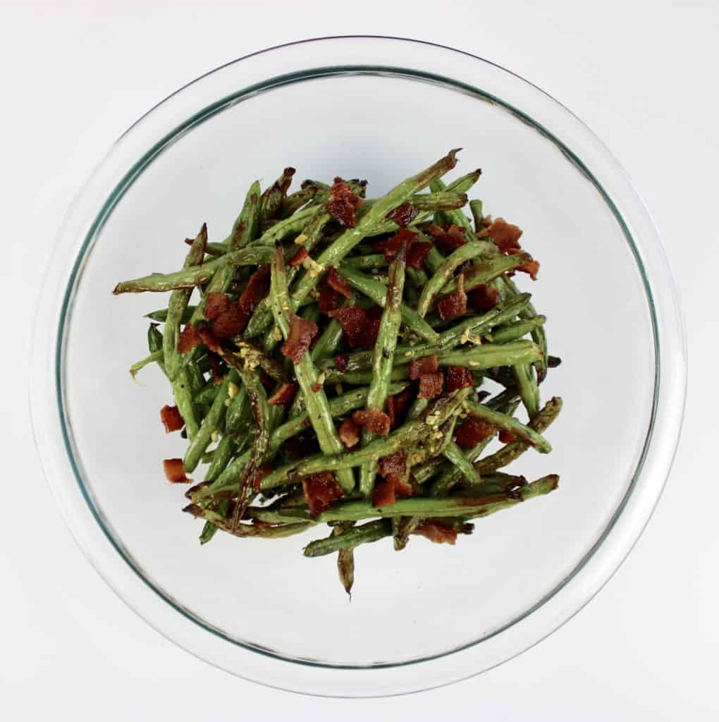 roasted green beans with crumbled bacon and garlic on top in glass bowl