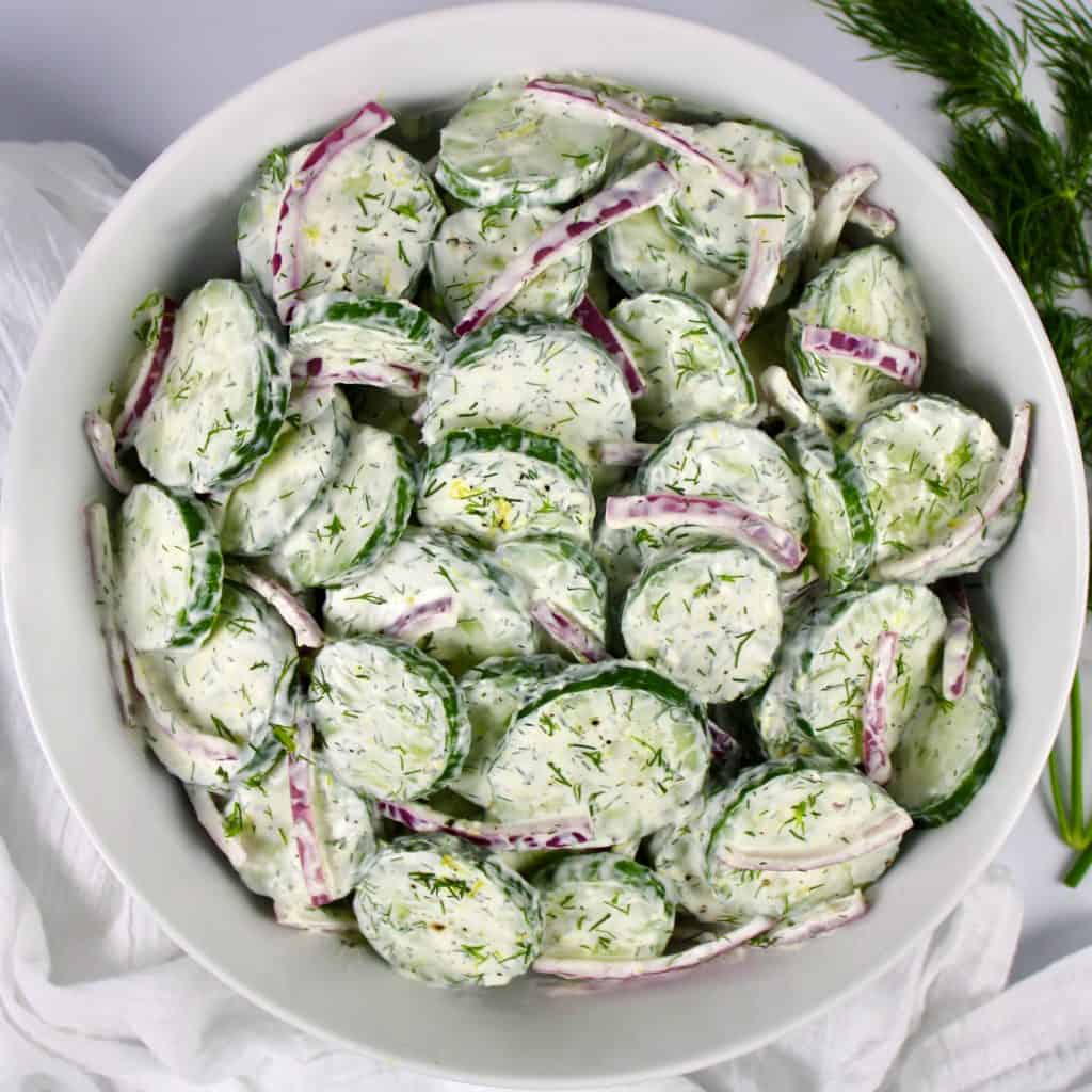 overhead view of Creamy Cucumber Salad in white bowl with dill on top