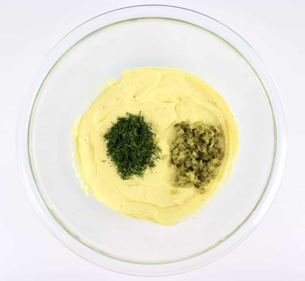 deviled eggs mixture in glass bowl with dill and chopped pickles on top