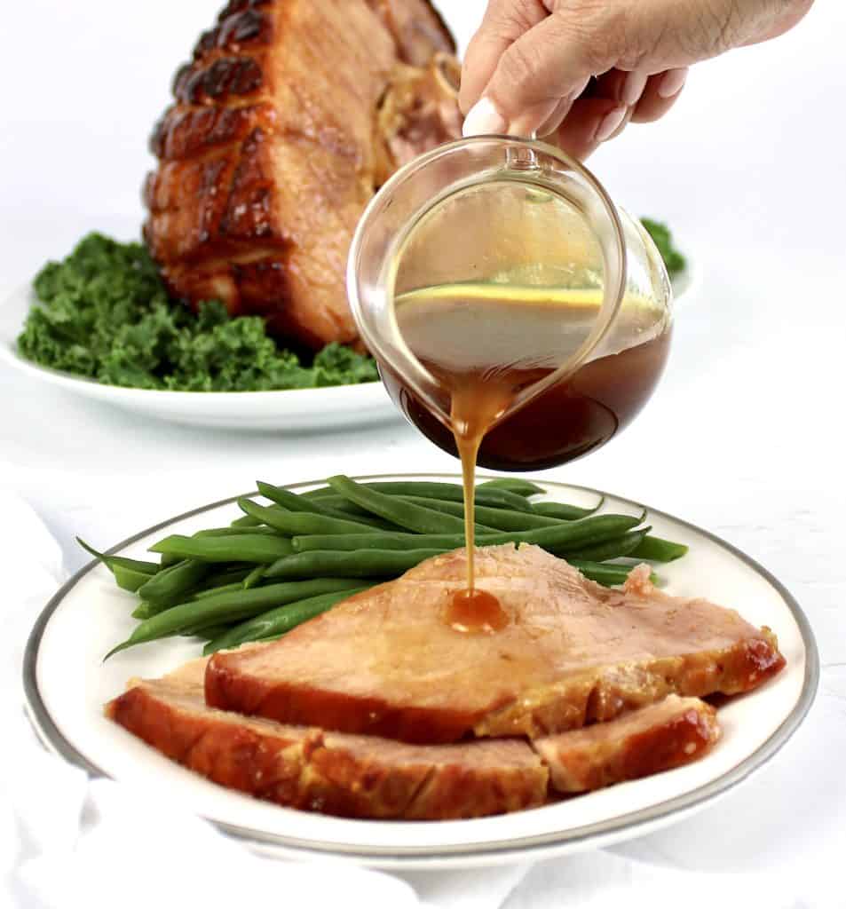 Keto Glazed Ham slices on plate with green beans and sauce being poured over top