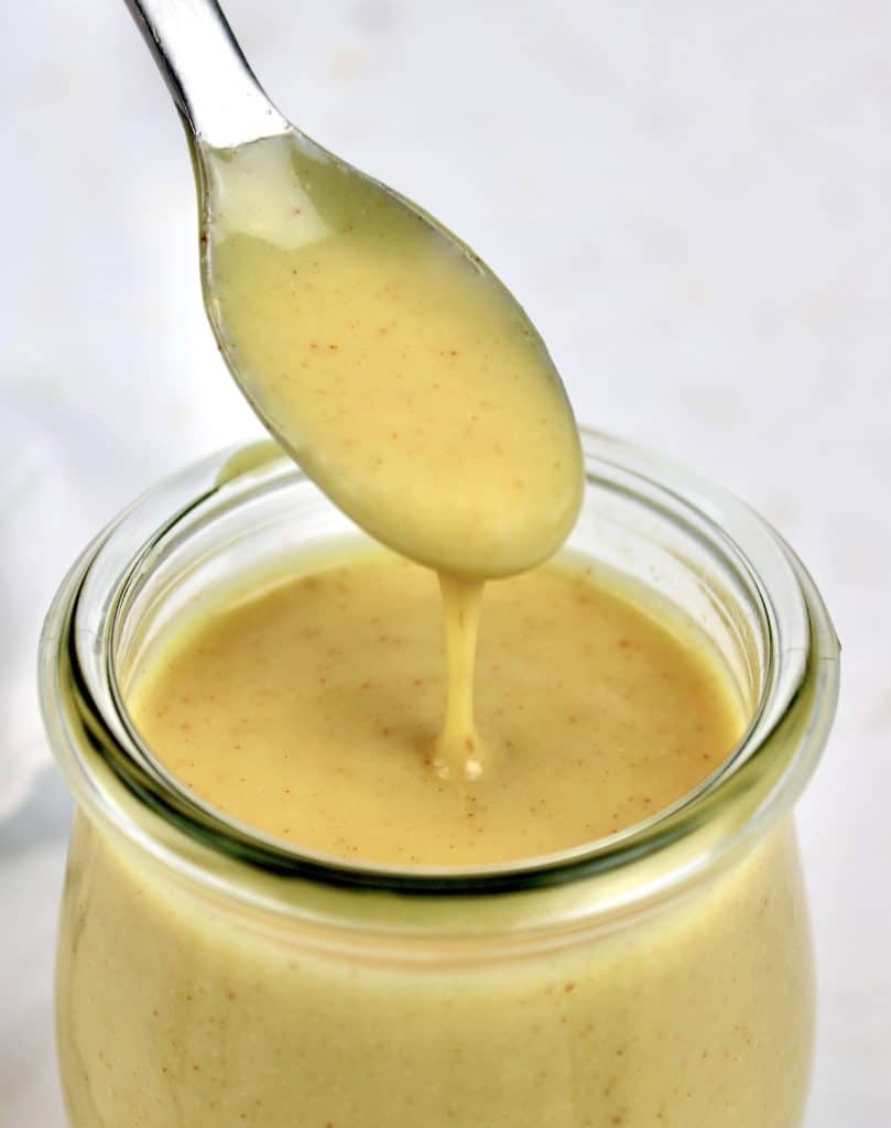 Keto Honey Mustard Sauce in glass jar being dripped off a spoon
