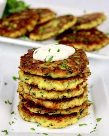 Keto Zucchini Fritters stacked on plate with platter in background