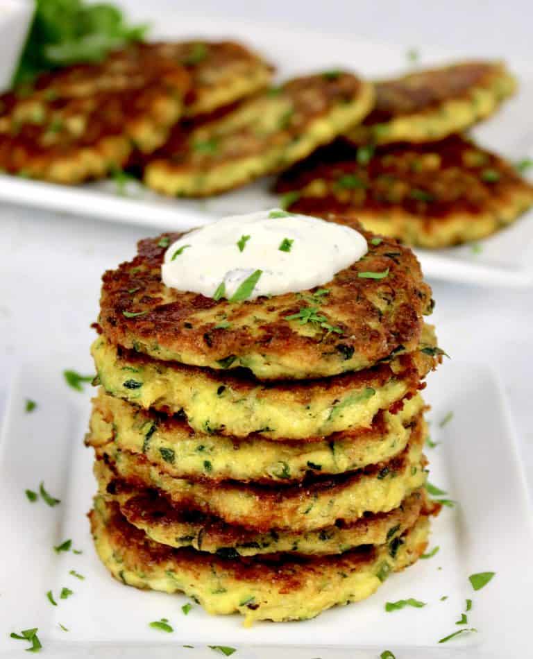 Keto Zucchini Fritters stacked on plate with platter in background