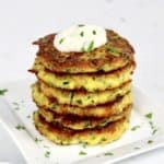 Keto Zucchini Fritters stacked up on white plate with dipping sauce on top