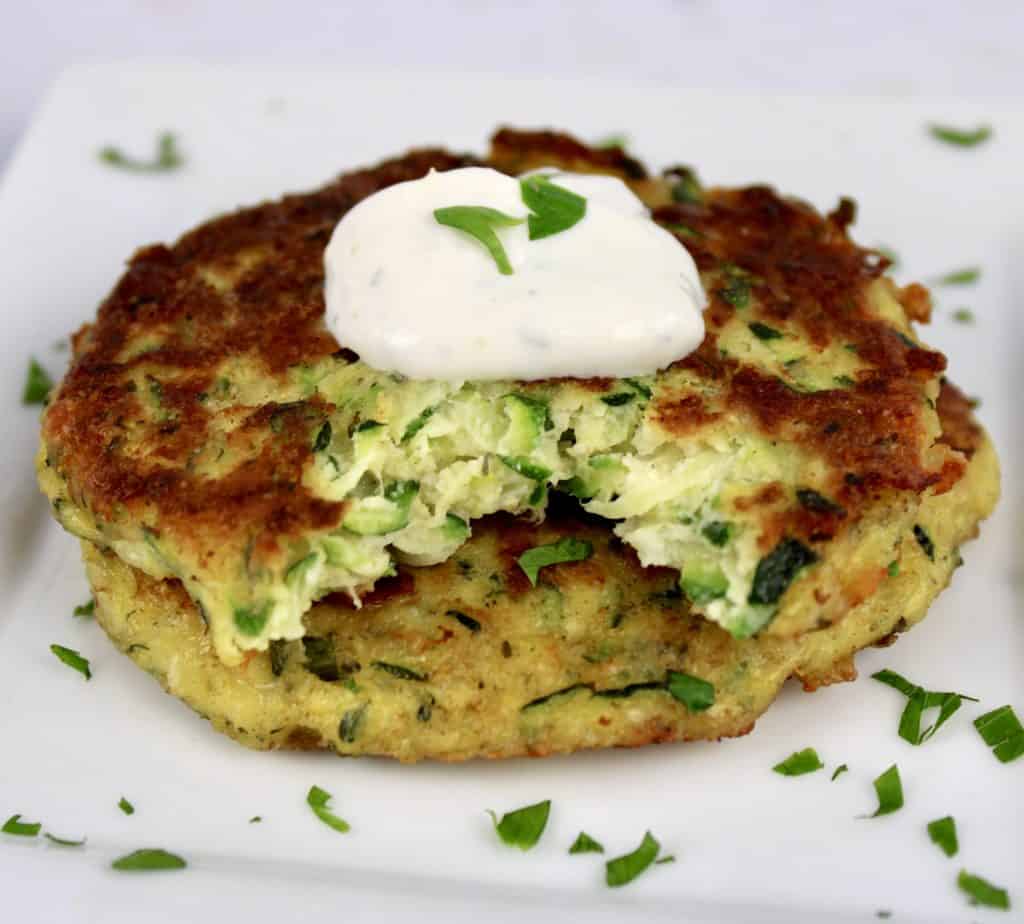 2 Keto Zucchini Fritters stacked on white plate with bite taken out of top one