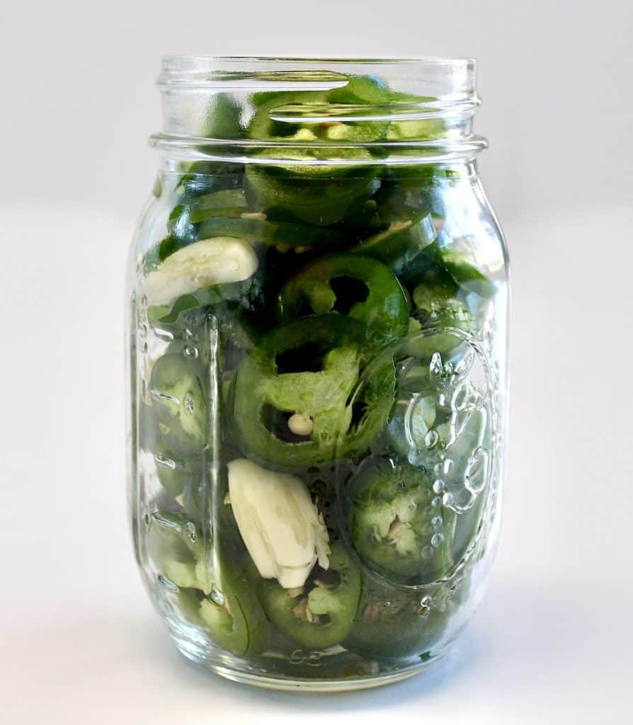 sliced jalapeno peppers in jar with garlic cloves
