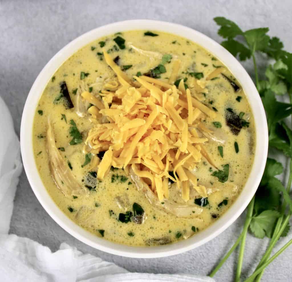 Slow Cooker Chile Relleno Soup in white bowl with shredded cheese on top