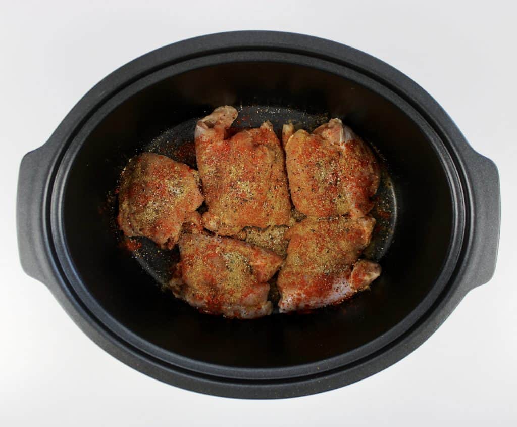 raw chicken thighs with spices on top in slow cooker insert