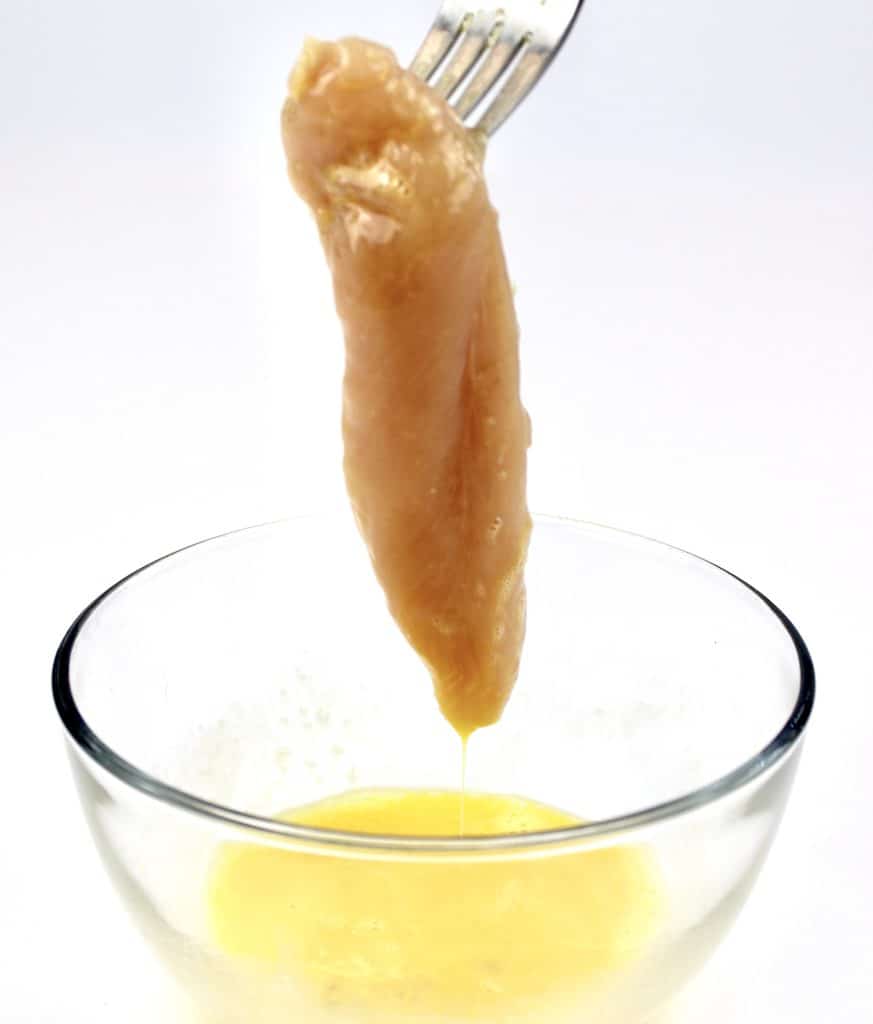 chicken tender being dipped into egg in glass bowl