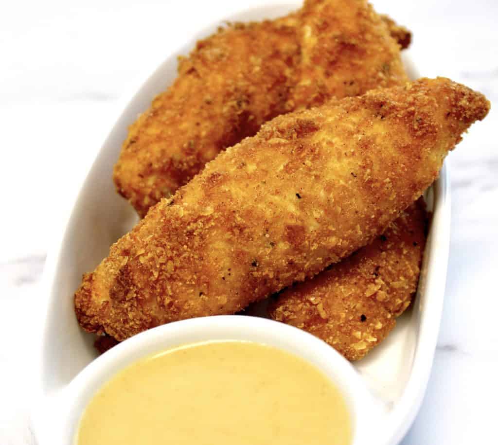 closeup of chicken tenders in white dish with honey mustard on side