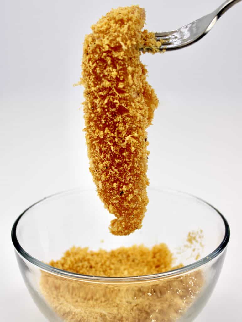 chicken tender being dipped into breading in glass bowl
