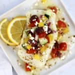 piece of cod with Greek salsa on top and lemon slices on side