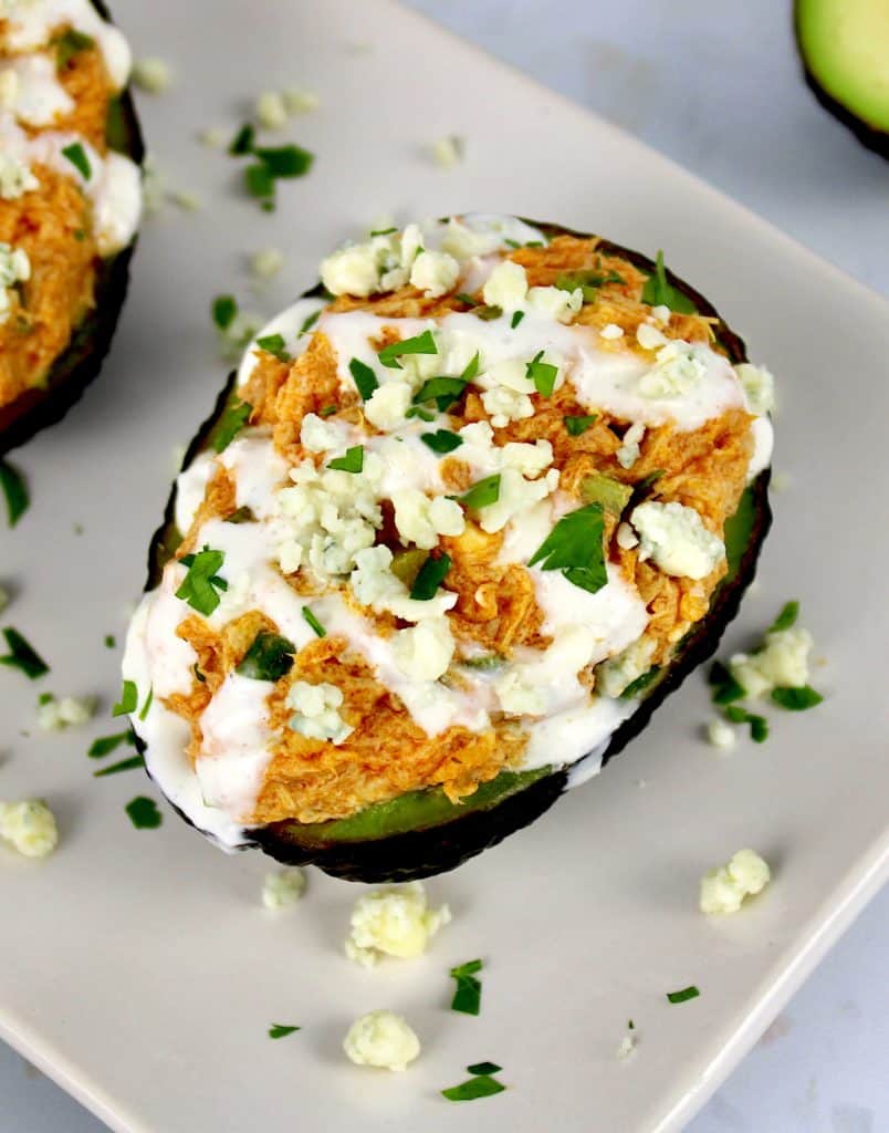 Buffalo Chicken Stuffed Avocados with drizzle of blue cheese dressing and crumbles on top