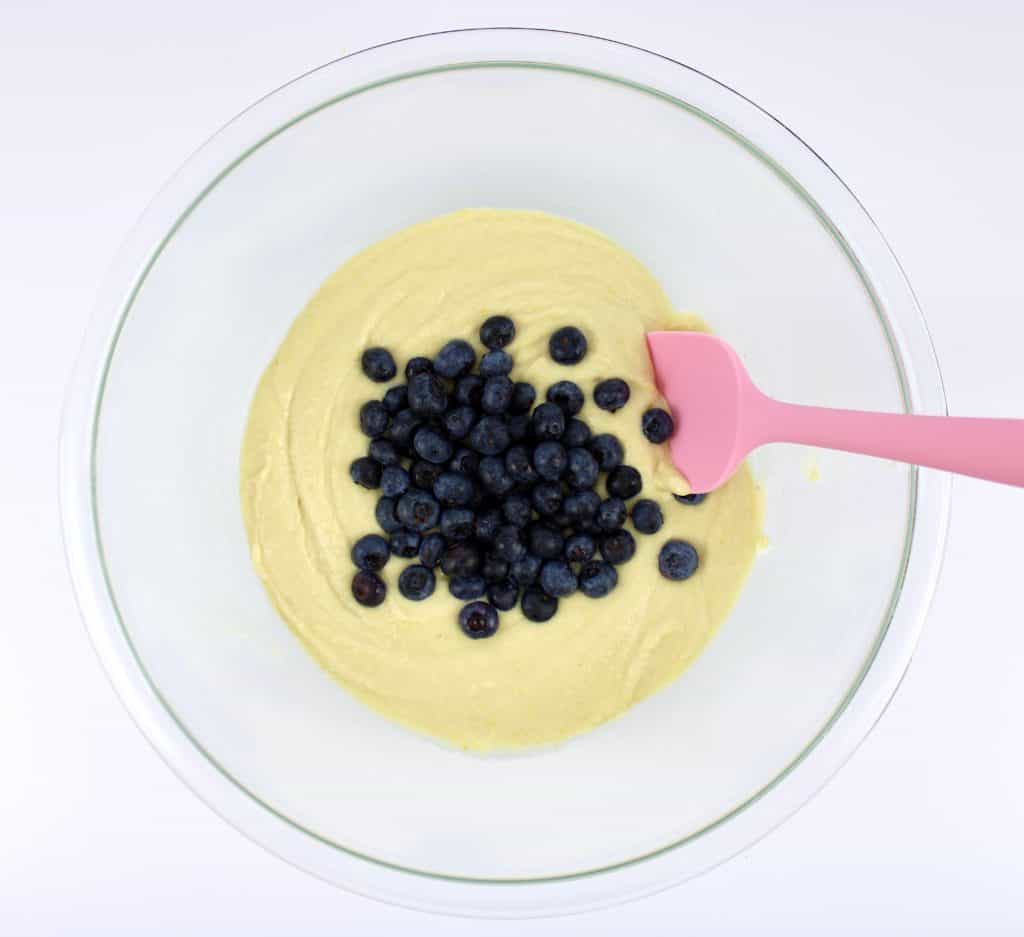 blueberry muffins batter with fresh blueberries and pink spoon in glass bowl